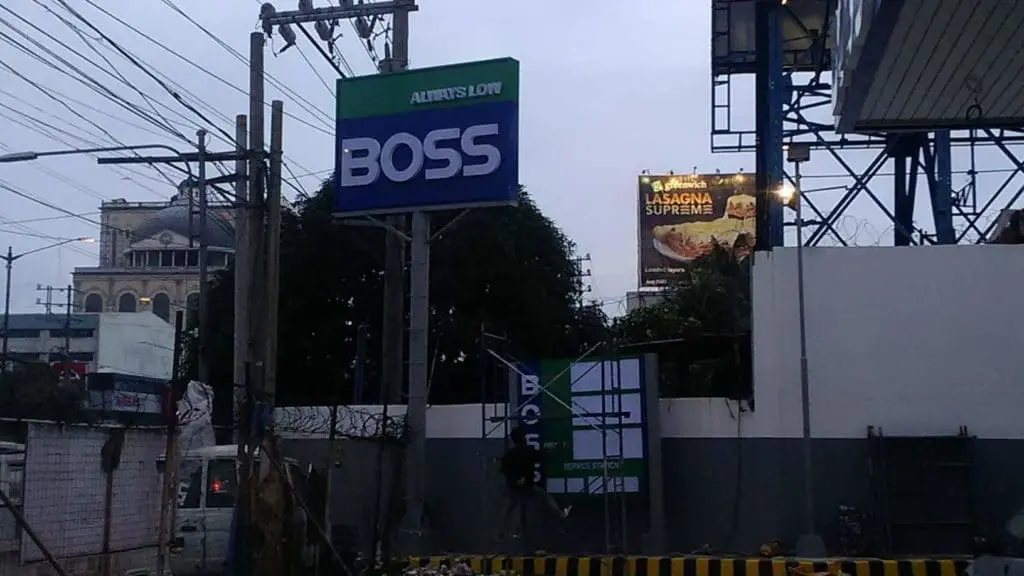Outdoor signage for BOSS in bold white on blue, near power lines and billboards in Ortigas, by M&G Global Ads.