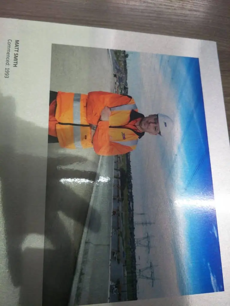 A man in a safety vest at a construction site near billboard signage in Makati, power lines and buildings behind, by M&G Global Ads.