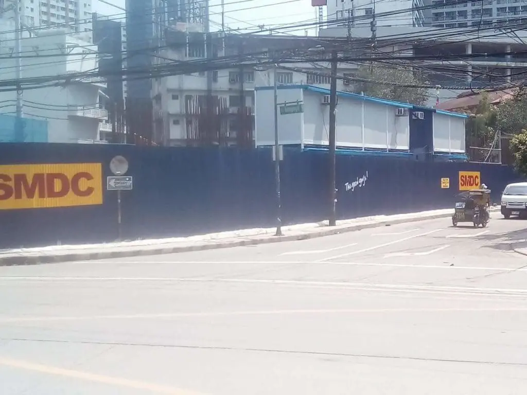 SMDC outdoor metal fence signage at a construction site in Makati with tricycle, buildings, and power lines by M&G Global Ads.