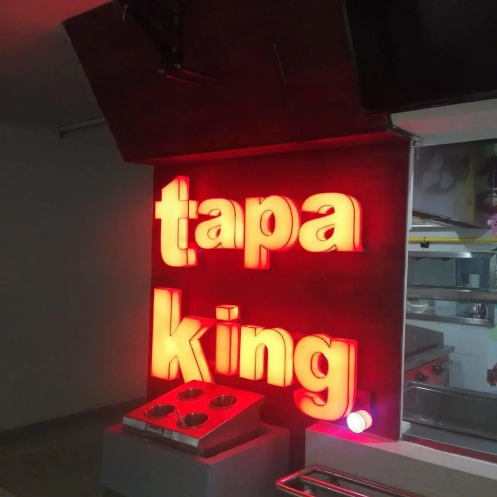 Tapa King acrylic signage in bright red on a dark indoor wall near a food counter, Quezon City, by M&G Global Ads.