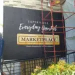 Large black building signage for The Marketplace in Makati, with red scaffolding and plants, by M&G Global Ads.