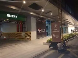 LED Pay Parking signage near garage entrance at night in Makati, bright lights, people walking. By M&G Global Ads.