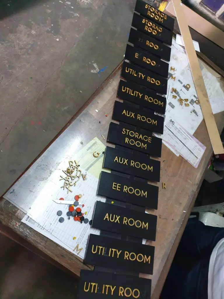 Black acrylic office nameplates with gold lettering for building signage in Makati, installation tools visible by M&G Global Ads.