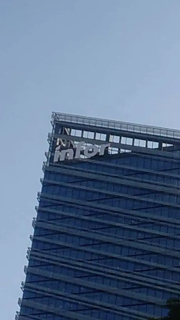 Damaged metallic building signage reading Inter atop modern glass office in Makati, clear sky, by M&G Global Ads.