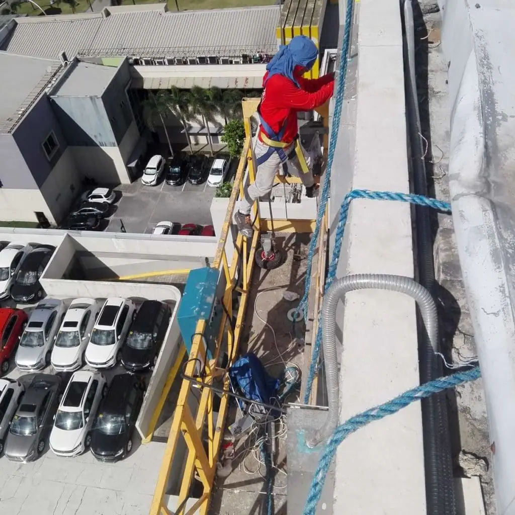 Installing acrylic signage on building facade in Ortigas, worker on scaffold above cars and buildings. By M&G Global Ads.
