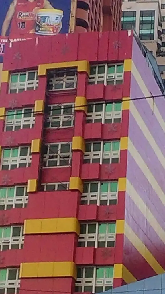 Striking building signage with red facade and purple stripes in Mandaluyong, partial billboard visible, by M&G Global Ads.