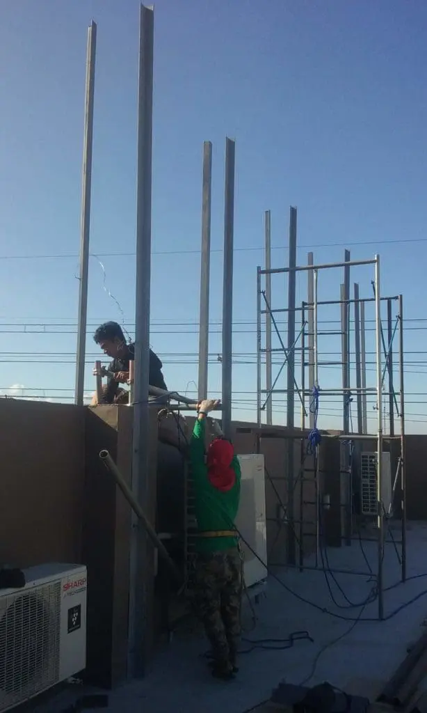 Installation of billboard signage rooftop metal beams in Makati by M&G Global Ads, two workers using ladder under blue sky.