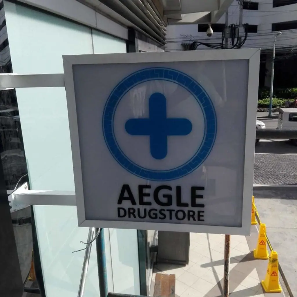 Metallic AEGLE DRUGSTORE signage with blue medical cross, mounted in Quezon City. Outdoor sign by M&G Global Ads.
