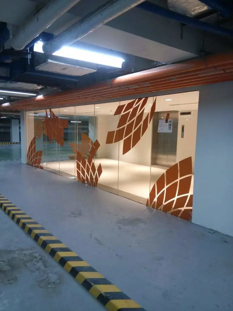 Acrylic signage in a modern building lobby with glass walls and orange patterns, Makati parking area view by M&G Global Ads.
