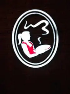 Metallic coffee shop sign in Makati: woman with ponytail holding steaming cup, red shirt detail. By M&G Global Ads.