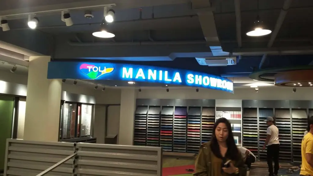 Illuminated LED signage for Toll Manila showroom in Makati, shelves with samples and people visible, by M&G Global Ads.