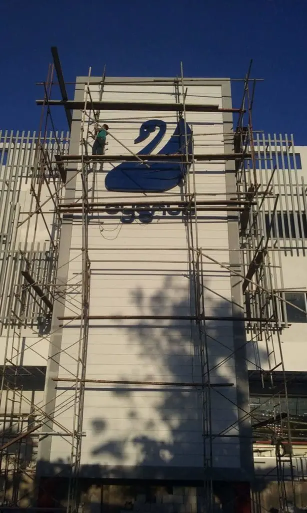Metallic swan signage installation for Swan in Makati, worker on scaffolding, clear sky backdrop by M&G Global Ads.