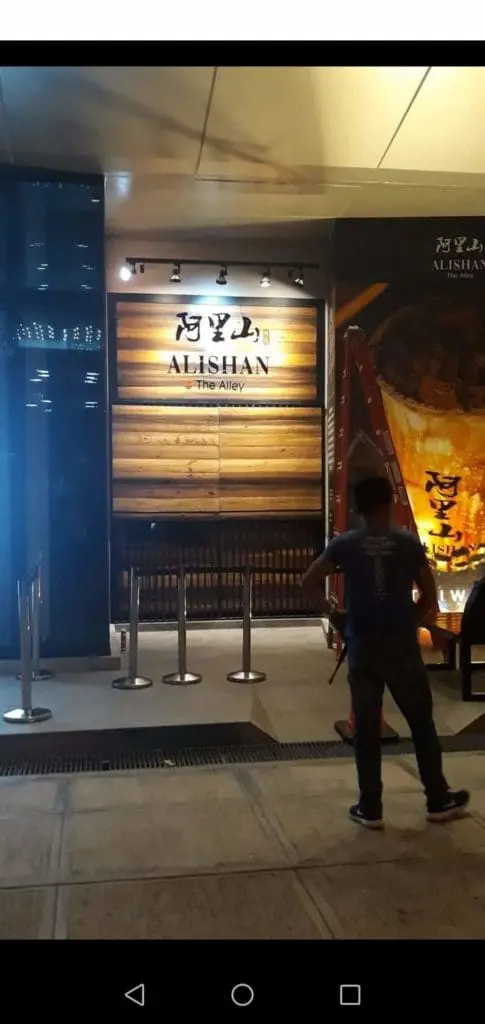 Alishan The Alley metallic storefront sign in Makati with wooden wall and barriers at night by M&G Global Ads.