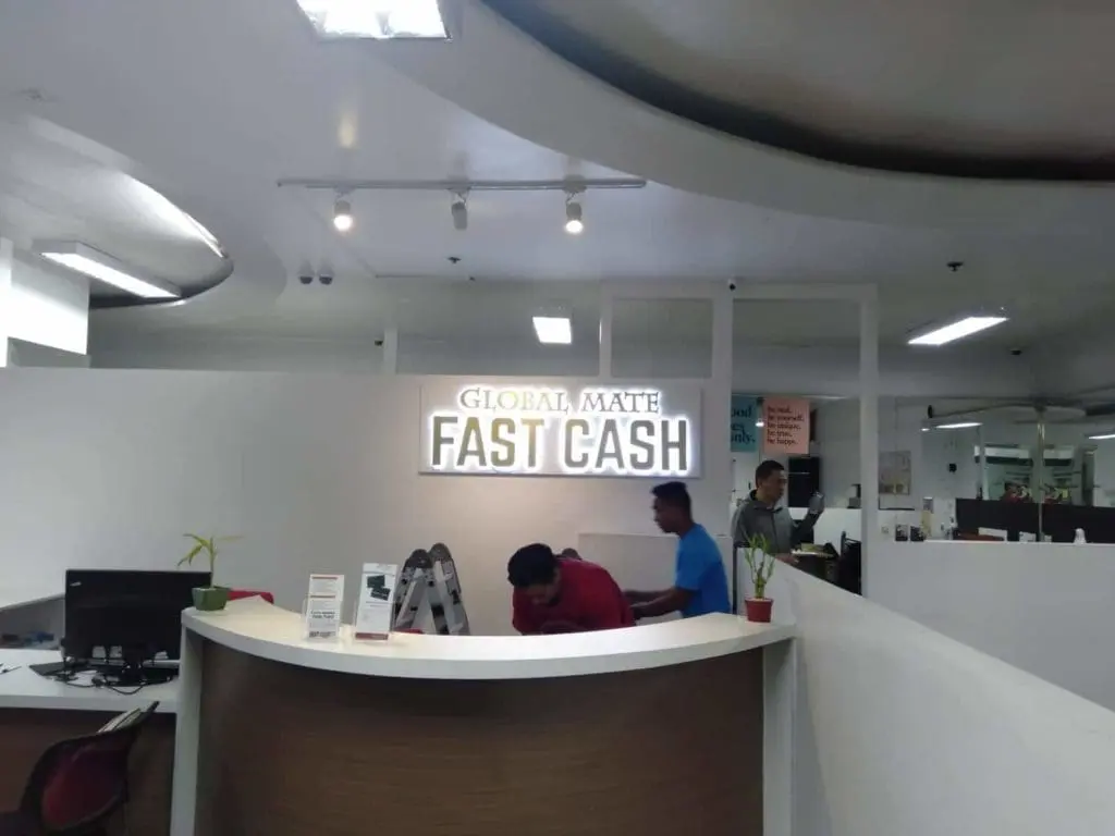 Illuminated acrylic signage for GLOBAL MATE FAST CASH in a modern office reception, Makati. Desk & 2 staff. By M&G Global Ads.