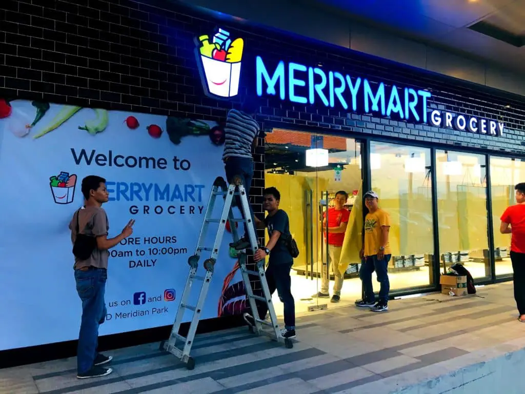 MerryMart Grocery metallic signage installation with welcome banner in Quezon City by M&G Global Ads. Four installers on site.