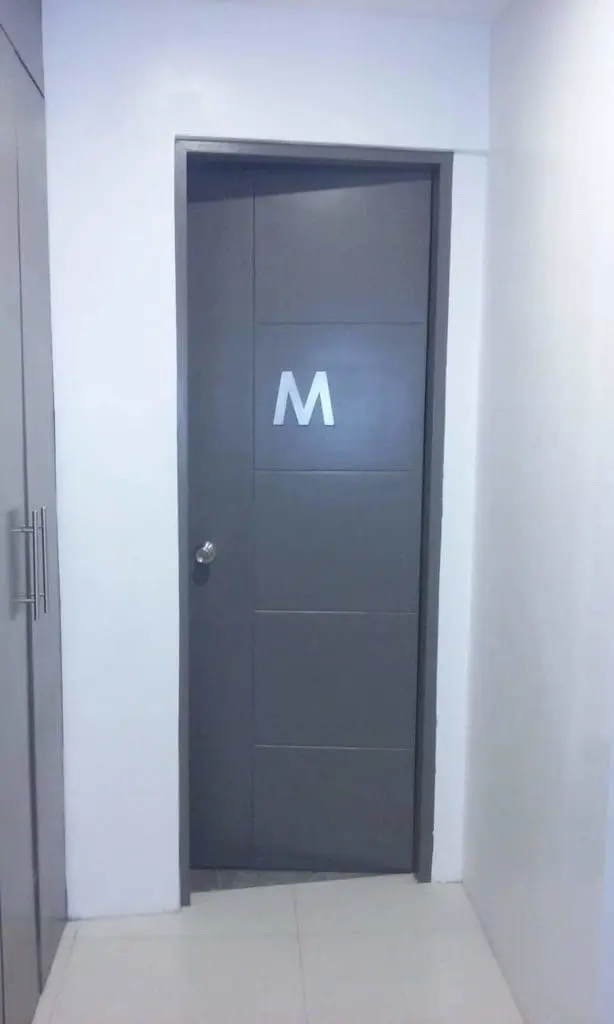 Mens restroom door with gray M signage in a tiled hallway, Ortigas location, indoor sign by M&G Global Ads.