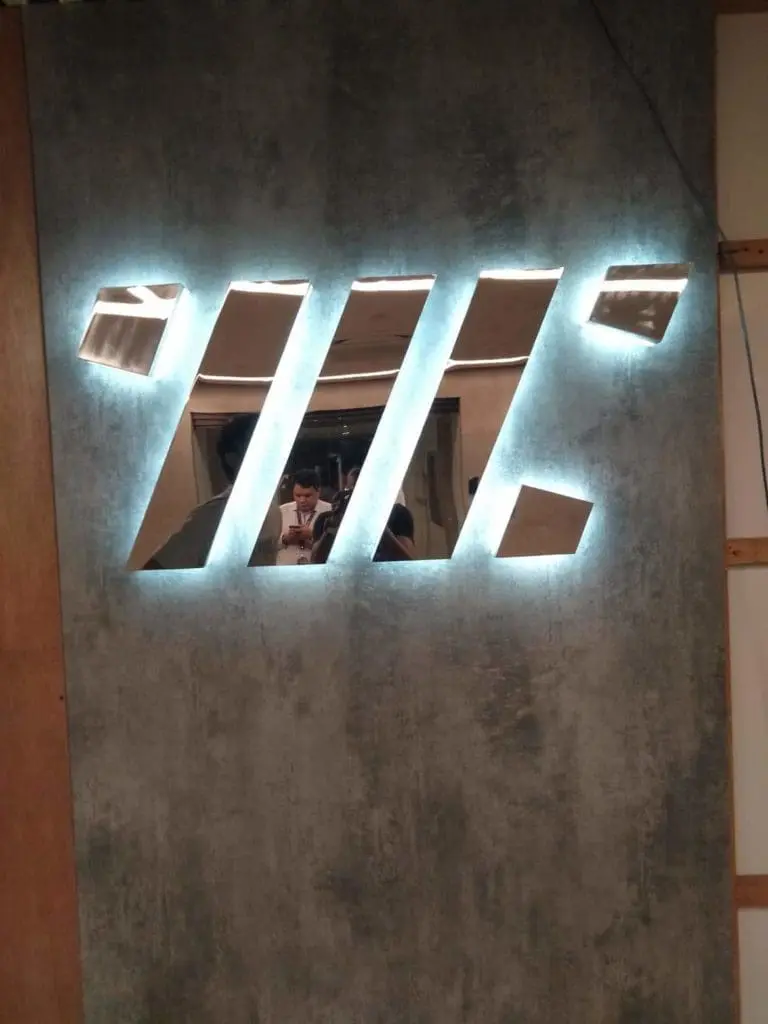 Modern LED signage with five illuminated angled cutouts on a gray wall, visible in Pasig—two people inside. By M&G Global Ads.