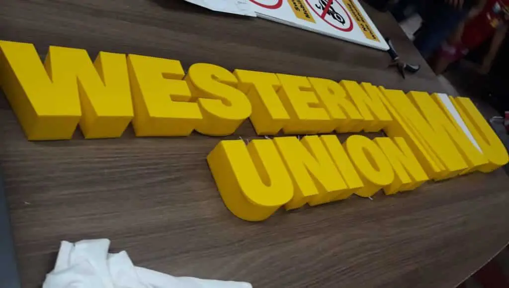Western Union 3D outdoor signage letters on wooden table in Makati, with papers and cloth nearby by M&G Global Ads.