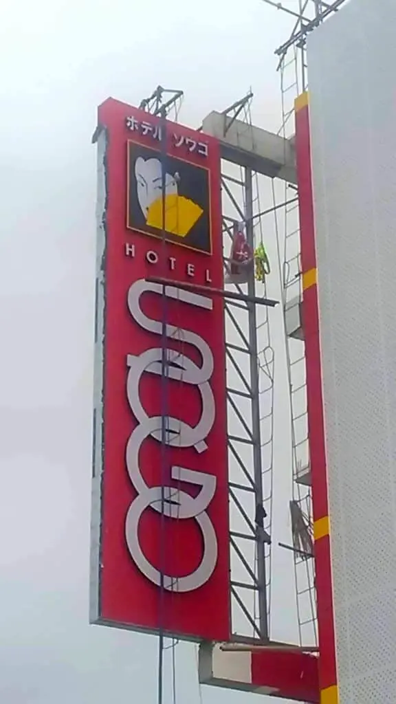 Outdoor building signage for Ugo with Japanese text and bird logo in Quezon City, cleaned by workers on scaffold by M&G Global Ads.