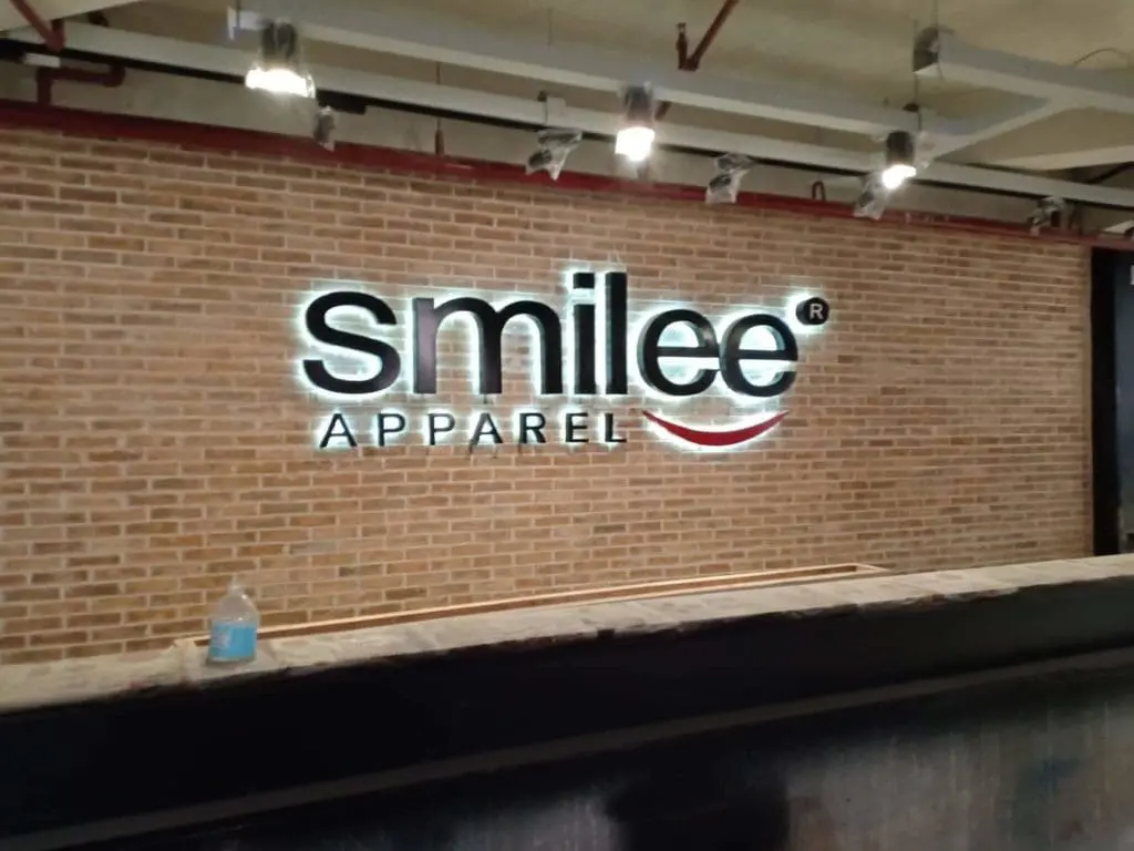 Glowing acrylic signage for smilee APPAREL on a brick wall in Makati, with red smile curve, by M&G Global Ads.