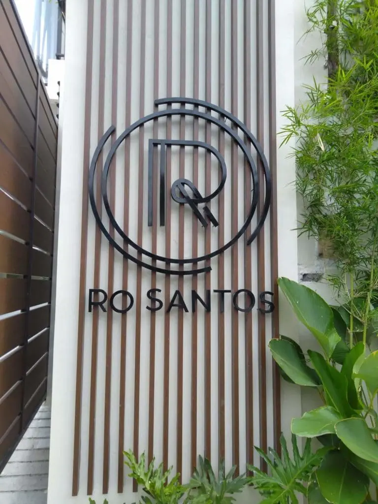 Indoor acrylic signage for RO SANTOS in Quezon City with stylized R and Q, wood slats, plants by M&G Global Ads.
