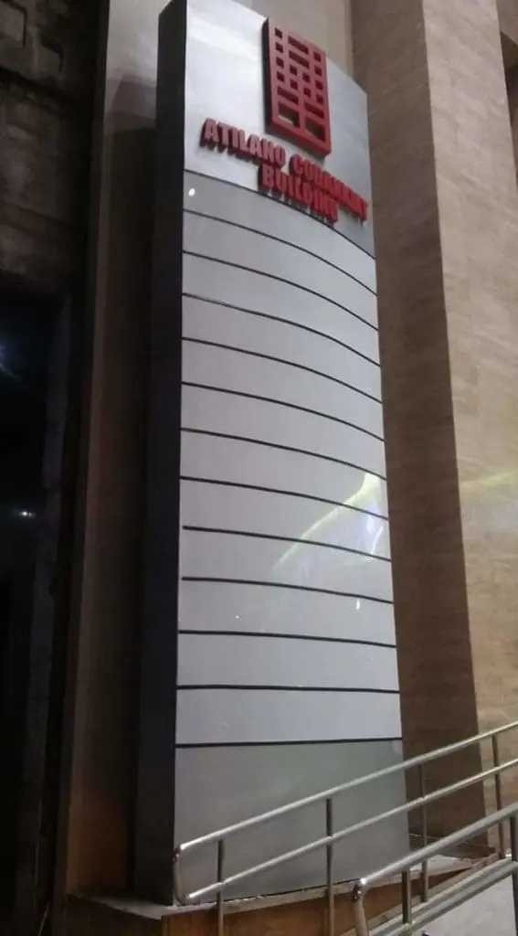 Atlako Corporate Building outdoor signage in Makati with horizontal lines and red logo, near stone wall and handrail by M&G Global Ads.