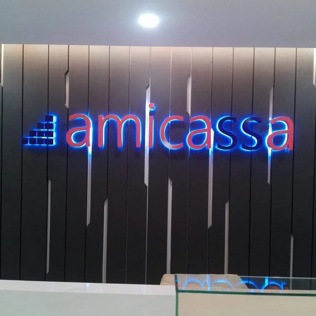 Amicassa blue and red LED signage in Makati on a dark vertical panel wall, counter with glass partition by M&G Global Ads.