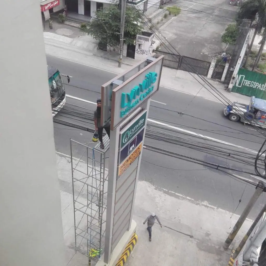 High-rise pylon signage installation for Lynville Residences in Quezon City, workers on scaffold by busy road, by M&G Global Ads.