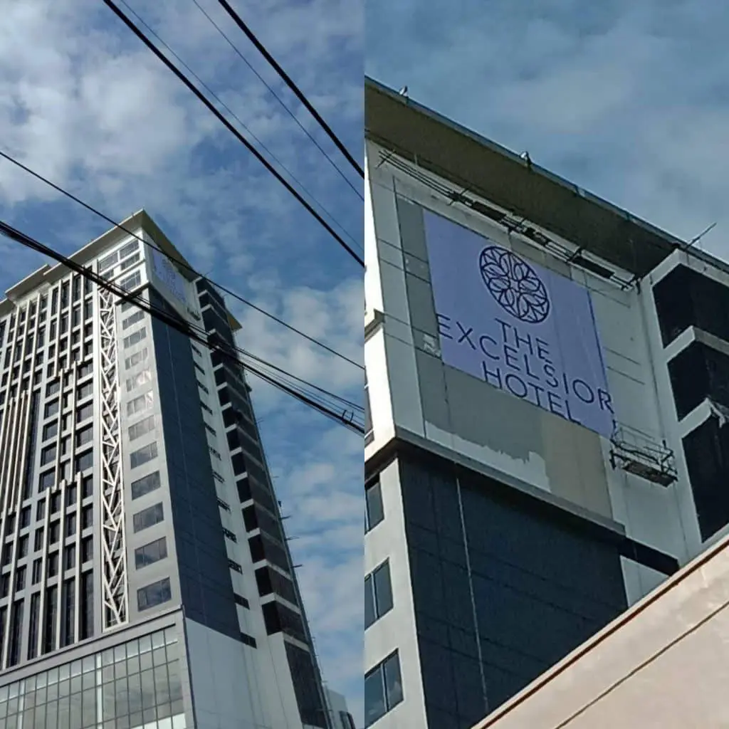 Metal signage for The Excelsior Hotel on tall building, large windows, power lines, Makati skyline by M&G Global Ads.