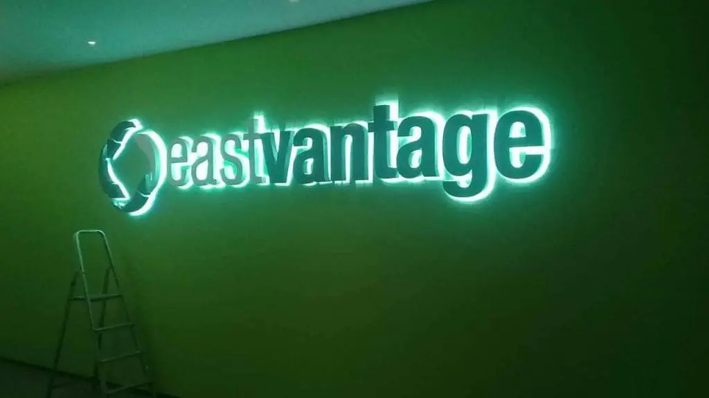 Illuminated LED signage with a circular logo on a green wall in Makati by M&G Global Ads; metal step ladder to the left.