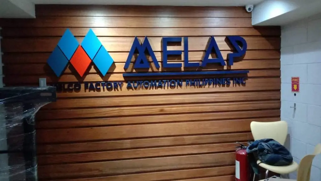 Blue acrylic logo signage for MELO FACTORY AUTOMATION PHILIPPINES INC., wooden wall, chairs, Ortigas. By M&G Global Ads.