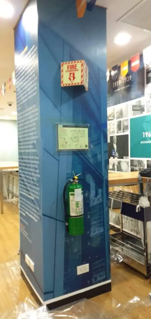 Acrylic signage on blue pillar with fire extinguisher, alarm box, outlet in Mandaluyong indoor space by M&G Global Ads.