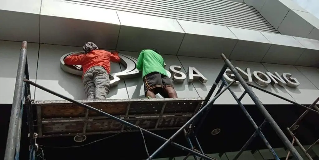 Metal sign installation for ASA GYONG in Makati, with two workers on scaffolding, by M&G Global Ads.