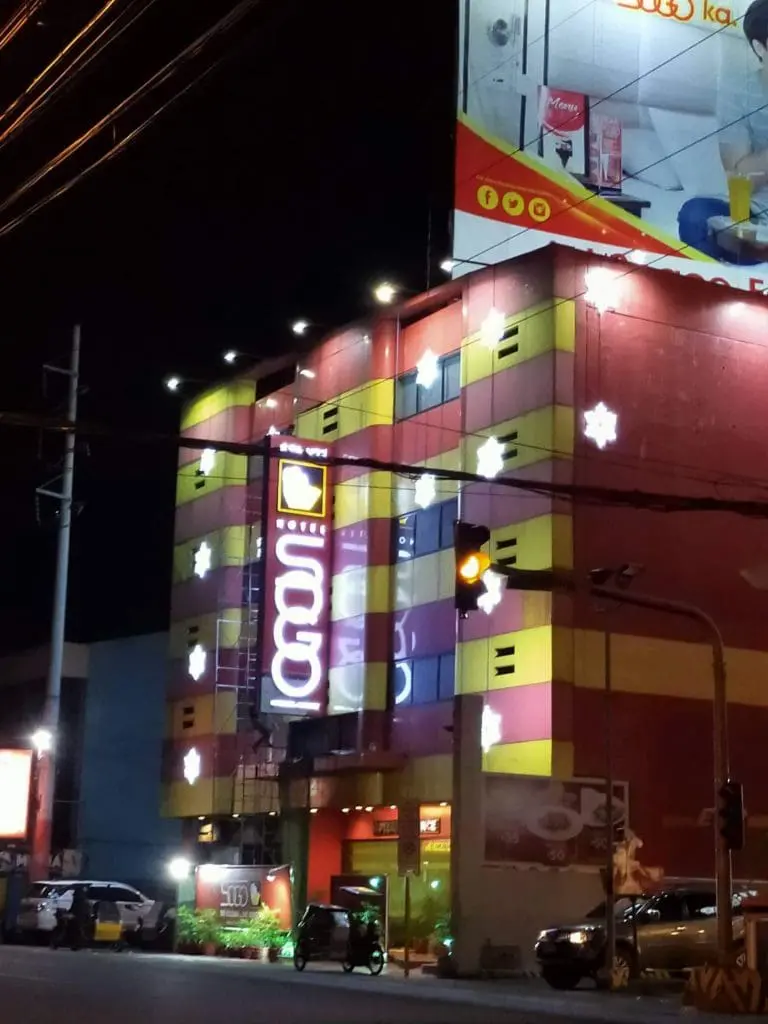 LED hotel signage glows on colorful facade in Ortigas at night, snowflake lights and cars in front; by M&G Global Ads.