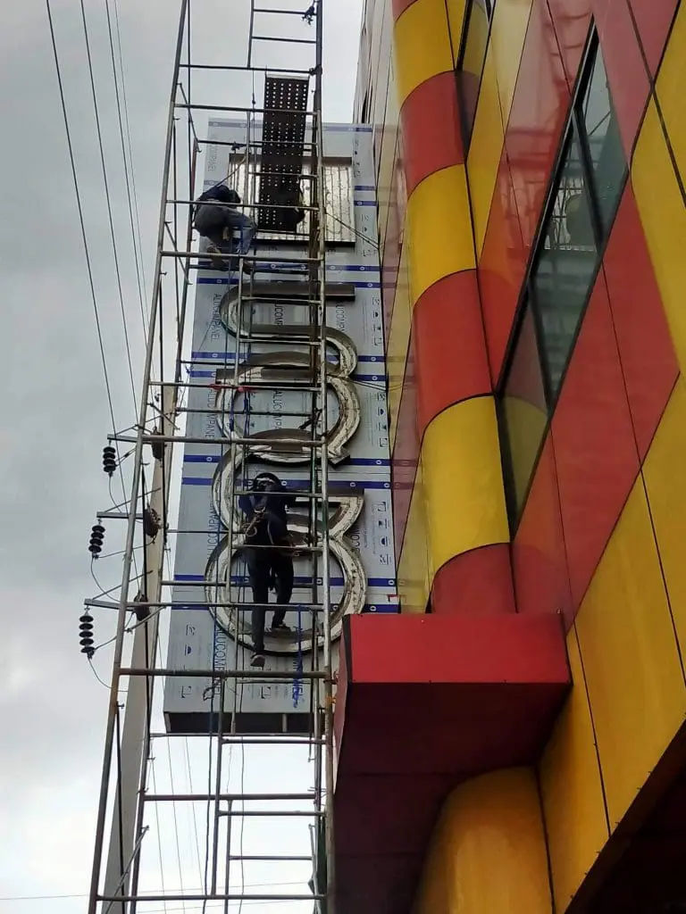 Workers installing large metallic outdoor signage on a yellow and red building in Quezon City by M&G Global Ads.