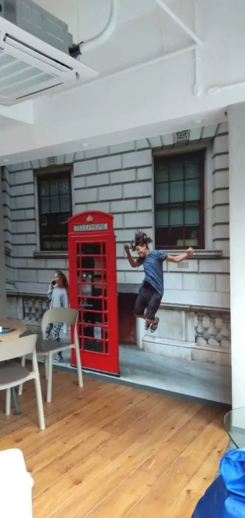 Wall mural of red British telephone booth and children, indoor decor signage, in a Makati room with wood flooring by M&G Global Ads.