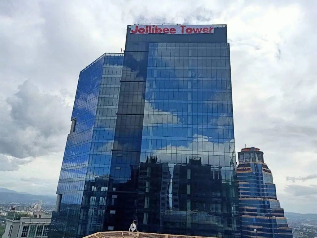 Jollibee Tower metallic outdoor signage in Ortigas, glass building reflecting clouds and cityscape—by M&G Global Ads.