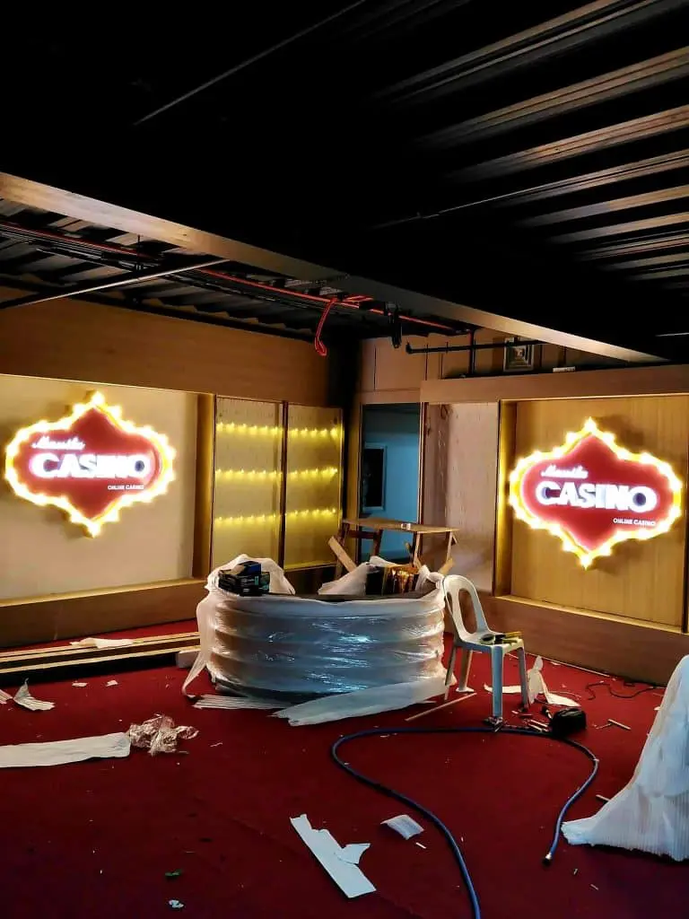 Illuminated acrylic casino signage in a Makati room under construction, red carpet, tools, exposed beams. By M&G Global Ads.