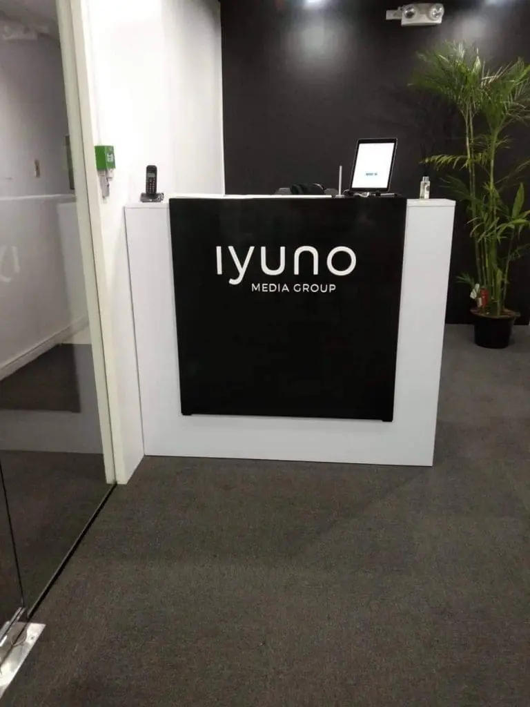 LED signage for Iyuno Media Group on a modern office reception desk in Makati, with monitor, phone, and plant by M&G Global Ads.