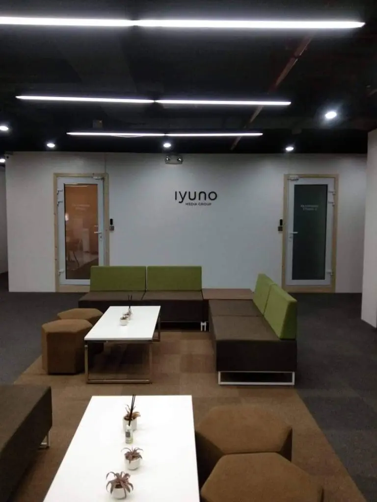 Acrylic signage iyuno media group in modern office lounge, Makati—modular seating, glass doors. By M&G Global Ads.