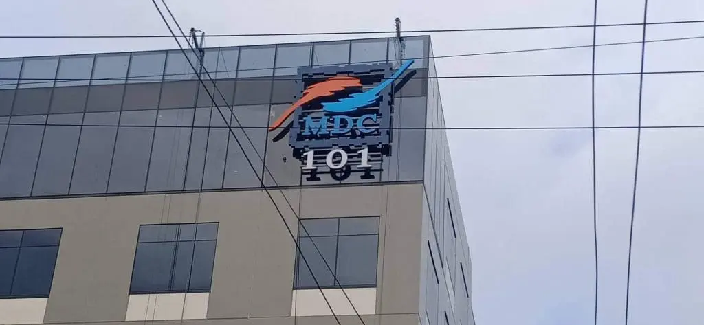Metallic outdoor business signage for MDC with orange and blue dolphin logo in Makati, by M&G Global Ads. Power lines in view.