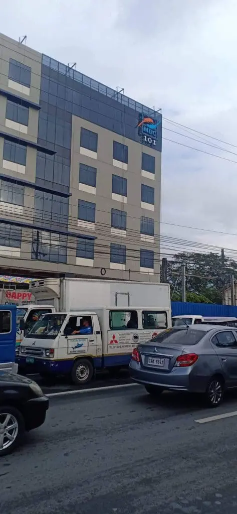 LED building signage for MDC 101 on a glass mid-rise in Ortigas with cars and power lines by M&G Global Ads.