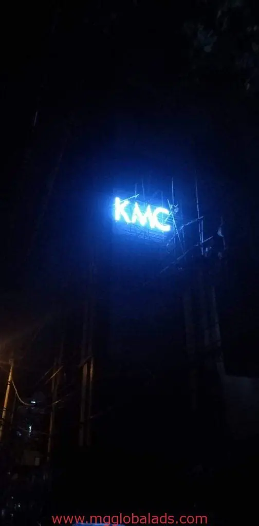 KMC blue neon building signage in Ortigas, mounted with scaffolding at night beside a streetlight by M&G Global Ads.