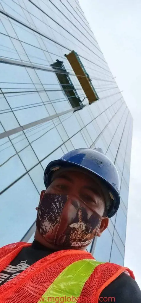 Construction worker selfie with metallic building signage in Makati, suspended platform above, by M&G Global Ads.