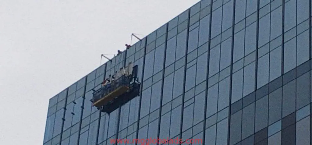 Workers clean glass windows near LED billboard outdoor signage in Makati, several floors high, by M&G Global Ads.