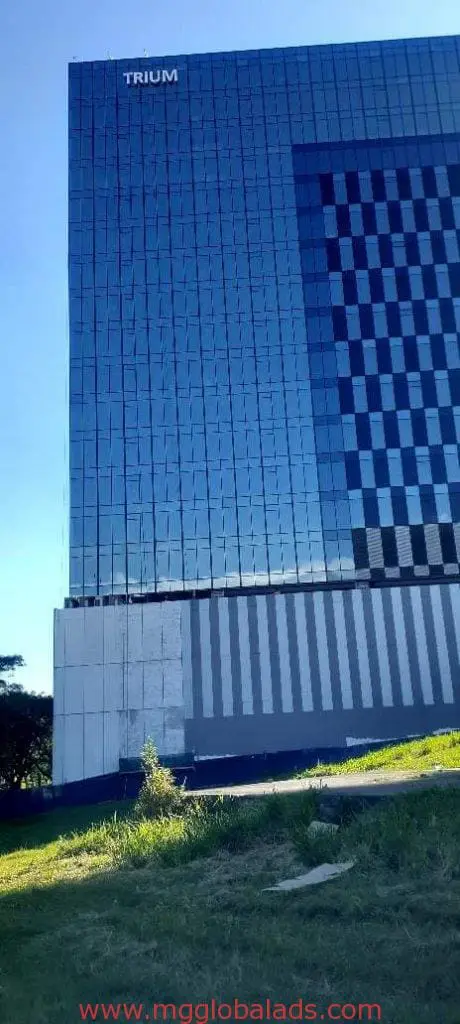 TRIUM bold building signage on modern glass office, Quezon City facade with panels and grass by M&G Global Ads.