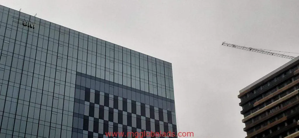 LED signage on geometric glass office building, construction crane, and dark tower in Makati by M&G Global Ads.