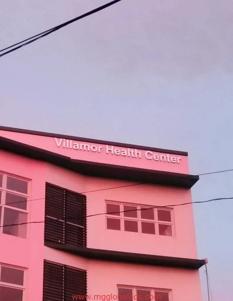 Acrylic signage for Villamor Health Center on pink building in Makati, large windows, dim sky. By M&G Global Ads.