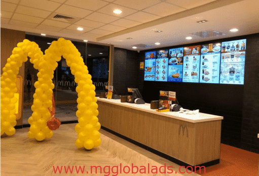 McDonald’s balloon arch signage with metallic signs at Makati counter, menu screens above. www.mgglobalads.com by M&G Global Ads.