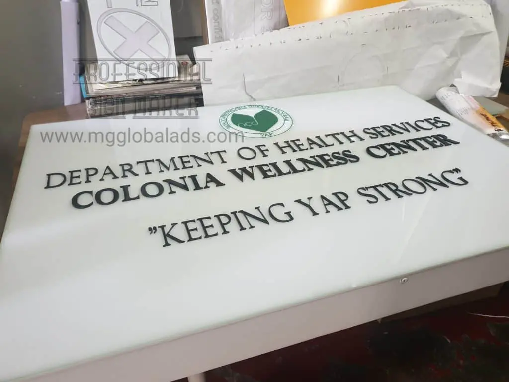 Metal sign for Department of Health Services client in Quezon City, with green logo and documents on table by M&G Global Ads.